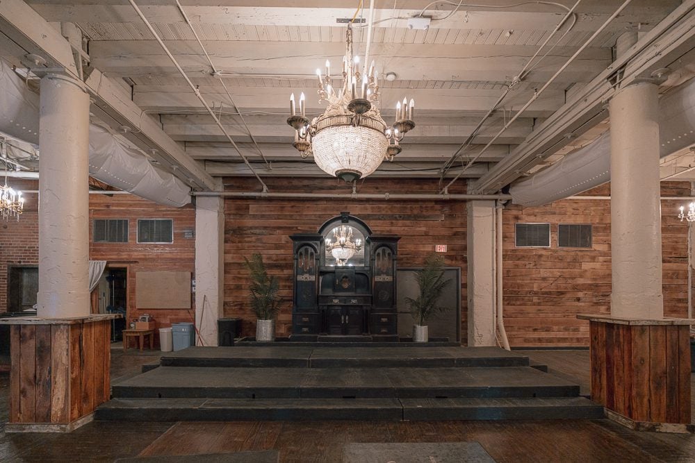 A photo of the Rumely. It features a large stage with a brass chandelier above it and wood paneling on the walls. 